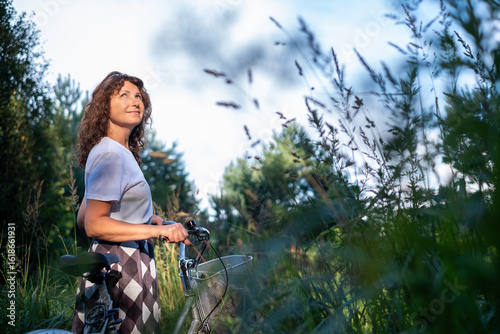 Foto Woman with curly hair stands beside bicycle in lush green field, enjoying nature