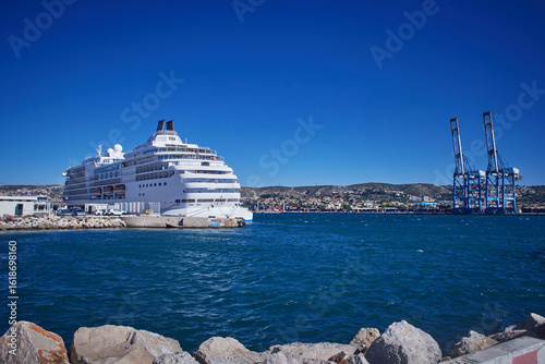 Large white cruise ship docked at harbor with blue sea and coastal town in background