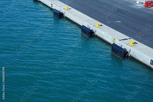 Empty modern pier with concrete fenders and bollards above calm blue water