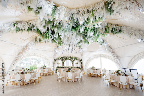 Elegant wedding reception hall featuring round tables, white and gold chairs, and floral arrangements