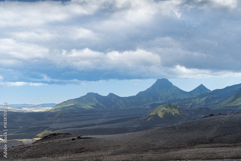 View of an expansive volcanic landscape under a cloudy sky, where jagged peaks meet dark, textured plains, Kirkjubaejarklaustur, Skaftárhreppur, Iceland. View of an expansive volcanic landscape under a cloudy sky, where jagged peaks meet dark, textured plains, Kirkjubaejarklaustur, Skaftárhreppur, Iceland.
