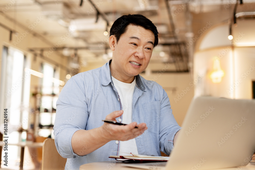 Fototapeta premium Asian businessman having video call and explaining something using laptop in cafe