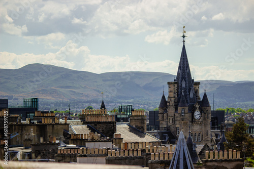 A panoramic view captures the historic skyline of Edinburgh, Scotland, under a partly cloudy sky