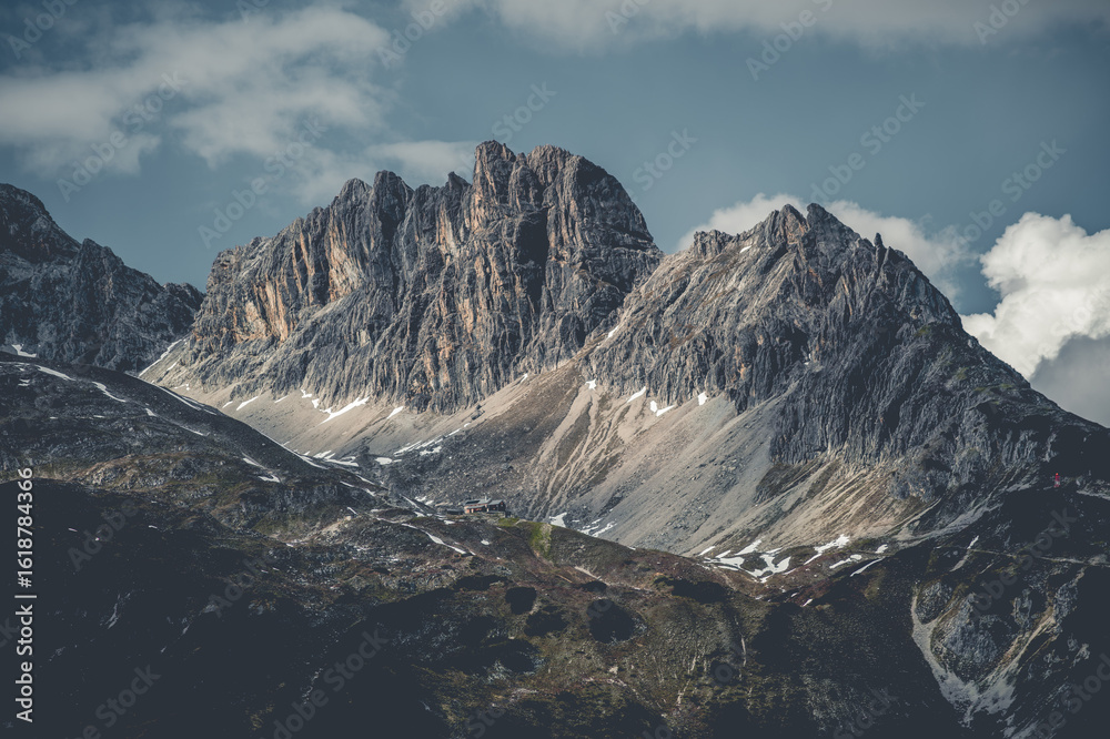Obraz premium The Hermann von Barth Hut sits at 2,131 meters, nestled among the rugged peaks of the Hornbach range in Tyrol, Austria. A scenic high-alpine refuge surrounded by dramatic mountain landscape.