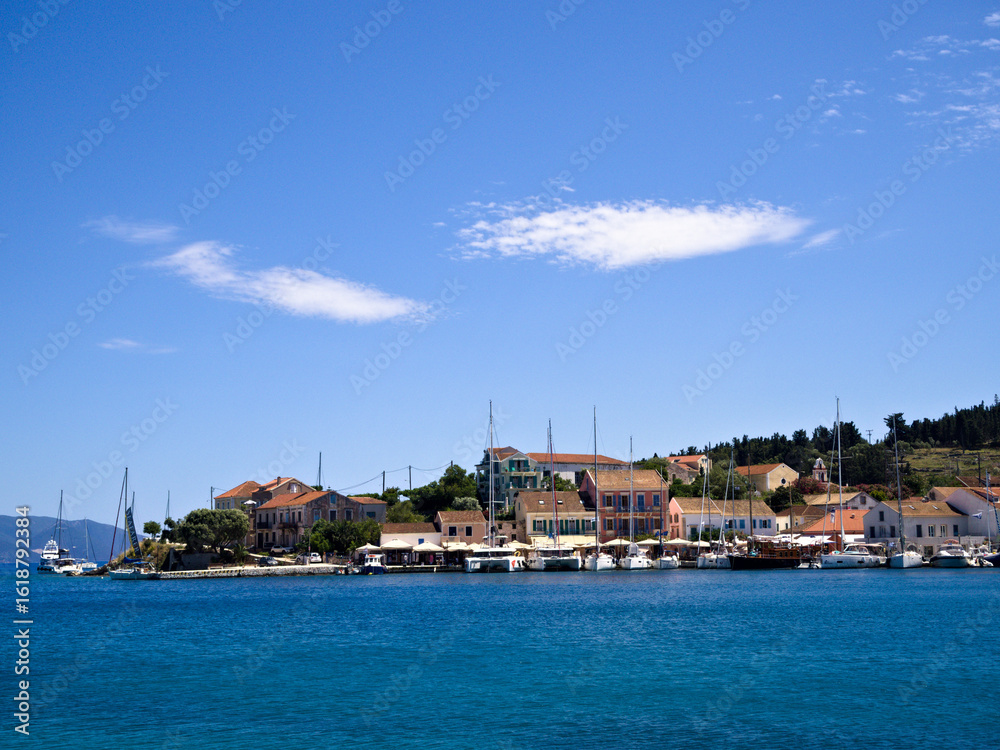 Obraz premium Bright day in Fiskardo, Kefalonia with boats and colorful houses, showcasing Greek island charm and summer mood.
