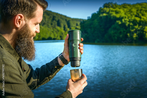 Man making coffee outdoors with a portable espresso maker by a mountain lake