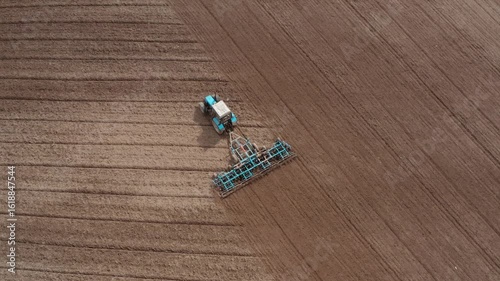 A tractor with a grain seeder is working in the field. Birds are flying around.