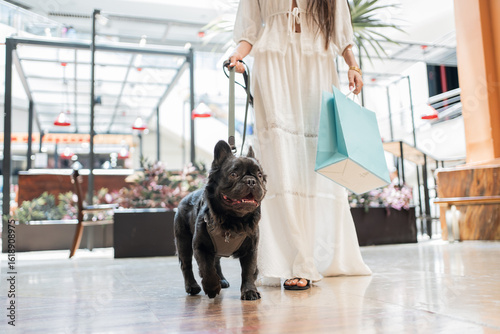 Close-up of a woman walking with her french bulldog in shopping mall after successful shopping