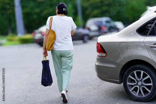Person walking with a bag in a parking lot during daytime near parked cars