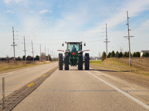 Tractor driving down a two lane asphalt road. Viewed from behind