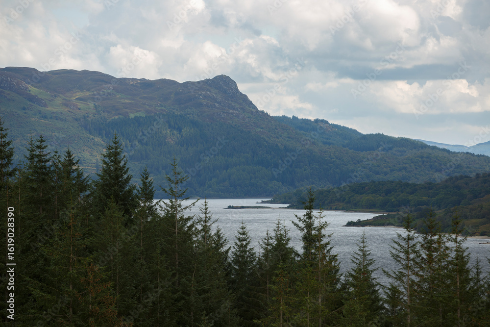 Naklejka premium Breathtaking view of a tranquil lake surrounded by mountains and evergreen trees in Scotland on a cloudy afternoon