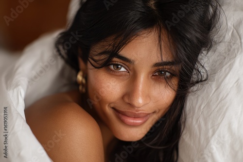 Smiling tan skinned brunette woman in bed with white sheets close up struggling to sleep