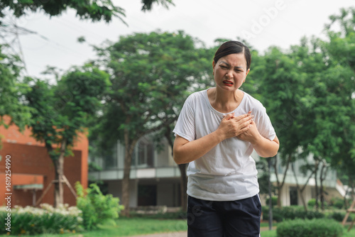 Tableau sur toile Woman clutches chest experiencing heart pain while outdoors in a green park sett