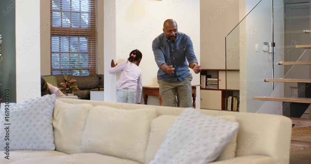 African American dad and daughter entering home dad waving daughter sitting on sofa pointing remote