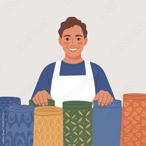 Smiling person in a white apron stands behind a row of colorful patterned cylindrical containers, possibly in a shop or workshop.