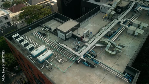 Detailed top-down view of rooftop HVAC layout including air conditioning units, tanks, ducting and insulated piping. Urban engineering solution for climate control on high-rise building.