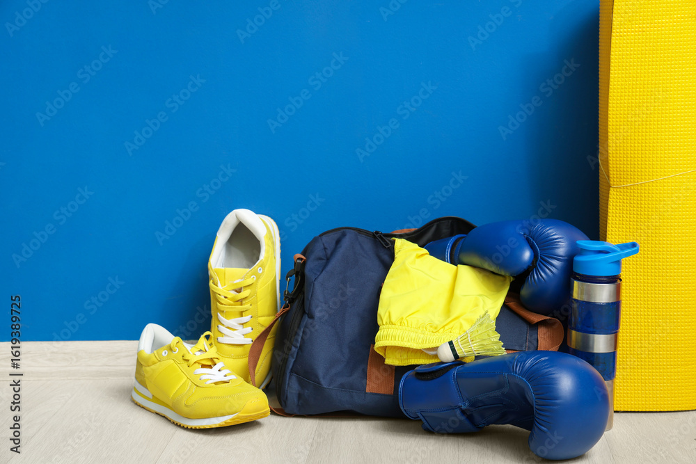 Fototapeta premium Boxing gloves, sneakers, yoga mat, sports bag and water bottle on floor near blue wall