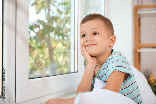 Thoughtful little boy near window in bedroom