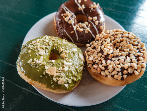 3 Donuts with varios flavour, chocolate, peanut and green tea donuts on the table, green background, top view, served by white plate