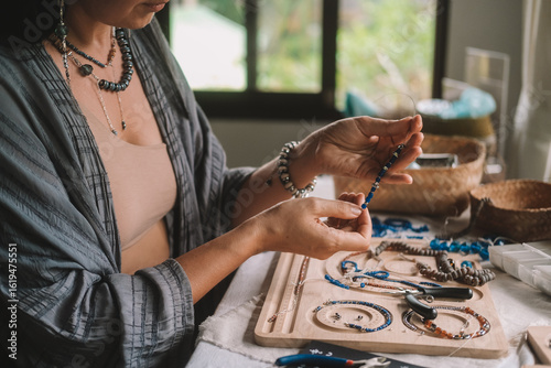 Close up of hands woman jewelry designer. She is sitting at a workspace with tools on it and is creating jewelry by stringing beads on fishing line. The process of creating jewelry. Small business. 