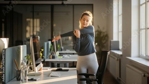 Young businesswoman doing stretching exercises beside her desk in bright modern office