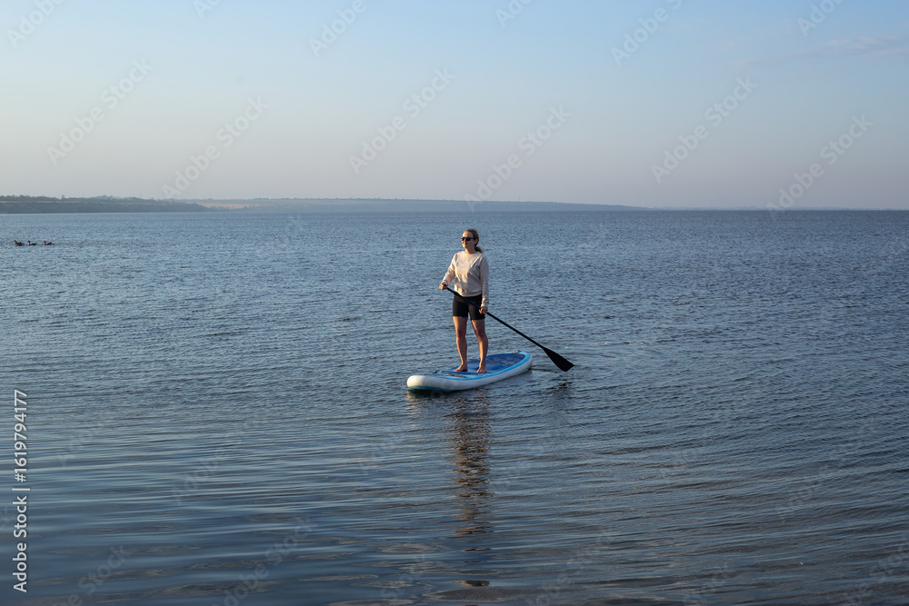 Naklejka premium Woman on sup board. A beautiful young woman relaxes on a SUP board. Standup paddleboarding
