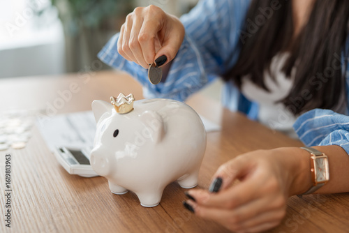 close up on adult woman hands put coins at piggy bank