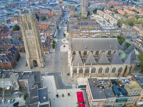 Aerial view of the historic Saint-Ã‰loi Church and its towering belfry cast long shadows on the cobblestone square, Dunkirk, France.