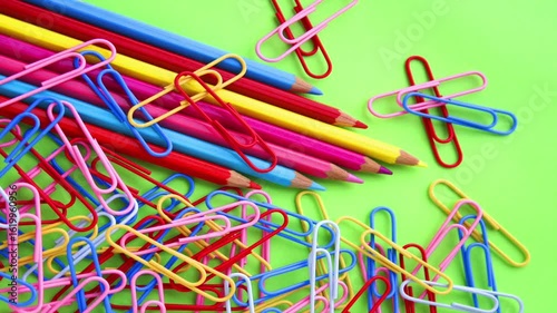Colourful pencils and paper clips on a green paper background