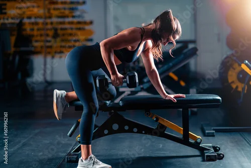 Panel kuchenny z motywem Biceps training with dumbbells engages a woman, lifting weights to build strength during a focused gym session.