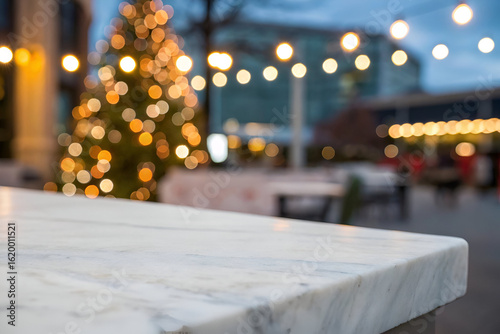 Blurred festive christmas tree with warm bokeh lights in an outdoor city setting, with a marble surface in the foreground