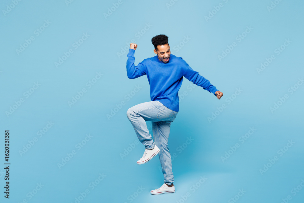 Full body young cool man of African American ethnicity wear sweatshirt casual clothes doing winner gesture celebrate clenching fists say yes isolated on plain pastel light blue cyan background studio. Full body young cool man of African American ethnicity wear sweatshirt casual clothes doing winner gesture celebrate clenching fists say yes isolated on plain pastel light blue cyan background studio.