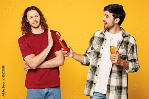 Fotografie Young strict sober happy two friends buddies men they wearing casual clothes together hold give bottle of beer refuse to take and drink isolated on plain yellow orange background