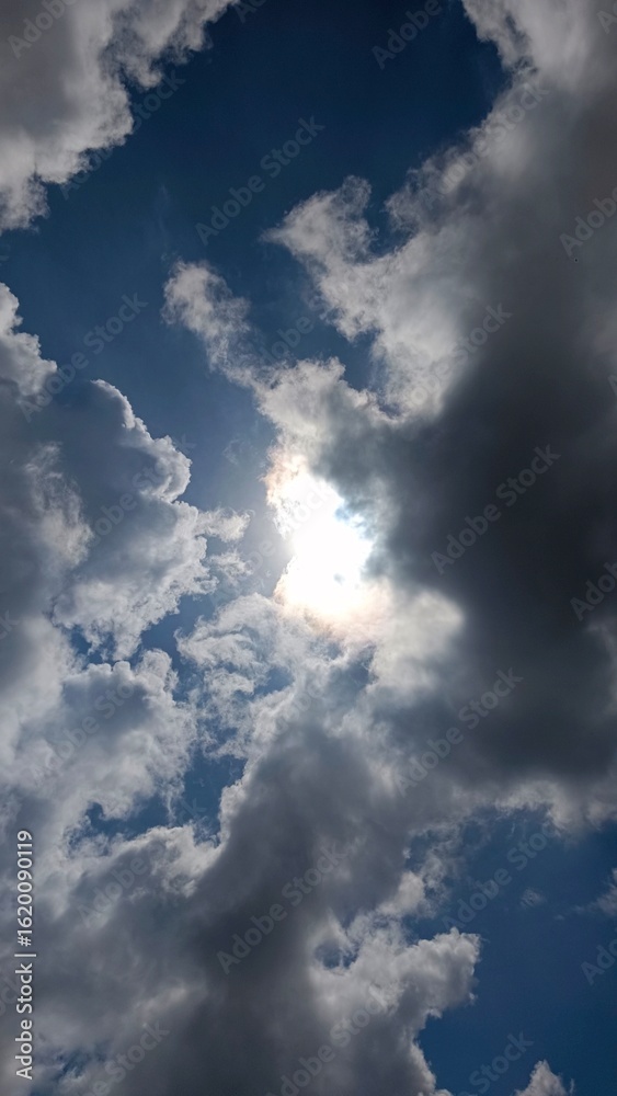 Fototapeta premium Bright sun hiding behind dramatic dark and white clouds in a blue sky