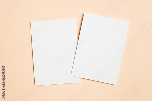 Two blank white sheets of paper on beige background, copy space for design purposes, ideal for invitation mockup presentations and creative projects