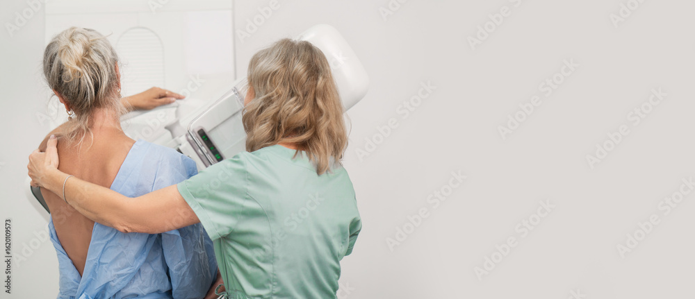 Obraz premium 50-year-old woman undergoes mammography procedure on special equipment mammograph with the help of assistant in modern clinic. Regular medical examination, screening for breast cancer copy space