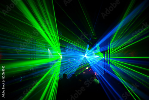 Laser beams in intense light green and bright blue in a dark  slightly foggy cave spread out in a star shape across the room during a dance event.