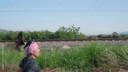 A woman trains by running alongside the train tracks as a train passes by her.
