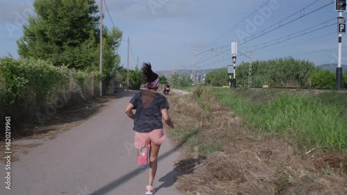 Rear view of a woman running and training next to a train track.