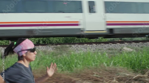 A train passes quickly as a woman does her daily workout next to the tracks.