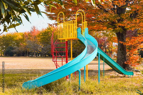 A colorful playground slide stands ready for children in a park during autumn.