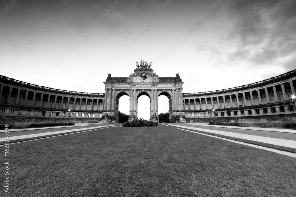 Obraz premium Brussels Belgium, panoramic black-and-white view of the Cinquantenaire triumphal arch and colonnades at dawn, empty park lawn in foreground, neoclassical landmark, travel architecture background.