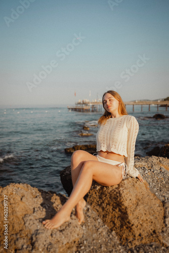 beautiful young girl with a beautiful athletic figure of European appearance in a swimsuit and underwear on the ocean shore in the open air. Sea waves and rocks with blue water. Travel and recreation