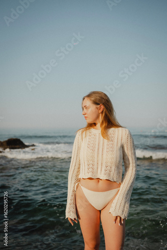 beautiful young girl with a beautiful athletic figure of European appearance in a swimsuit and underwear on the ocean shore in the open air. Sea waves and rocks with blue water. Travel and recreation