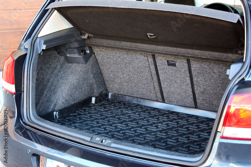 Open car trunk with dark carpeted lining, textured black rubber mat, and a red fire extinguisher mounted on the right, showing organized storage space in a blue hatchback