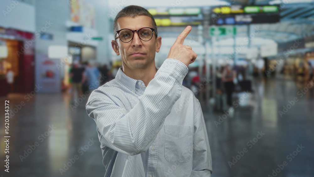 Fototapeta premium Man pointing in busy airport with people blurred in background suggesting travel, confusion for navigating terminal