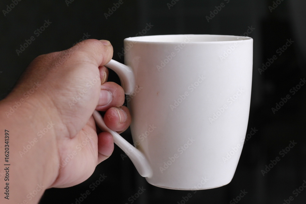 Obraz premium Hand holding a large white cup on a black background.