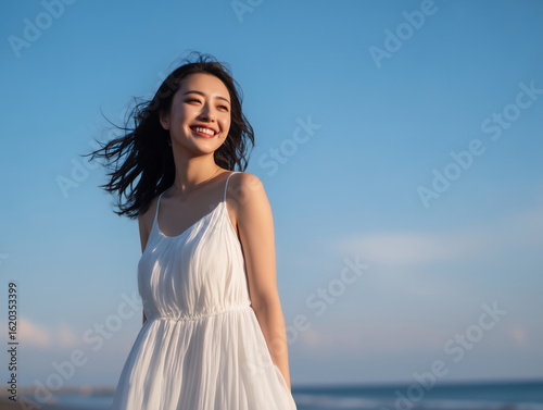 夏の海辺で風になびく白いワンピースの日本人女性ポートレート