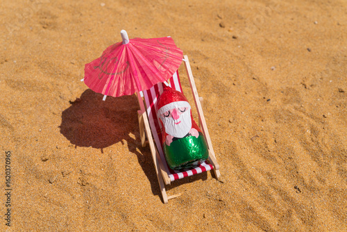Wallpaper Mural Chocolates Santa sits upright on beach chair, figure shaded by wide paper umbrella. Christmas in July concept Torontodigital.ca