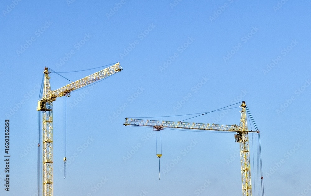 Construction cranes against blue sky, minimalistic industrial photography Construction cranes against blue sky, minimalistic industrial photography